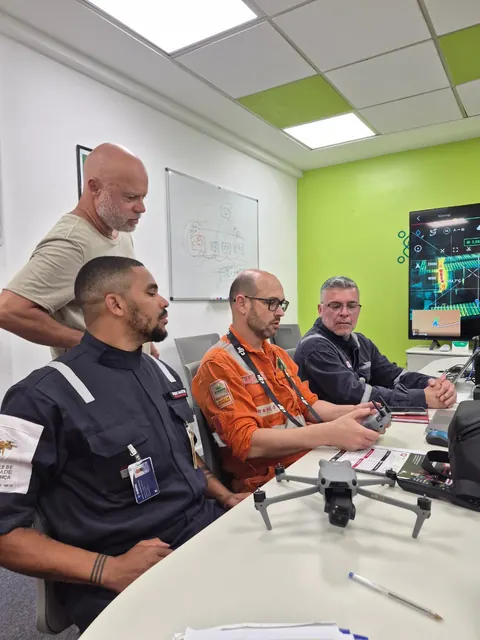 Alunos de macacão laranja em sala de aula, com o drone sobre a mesa